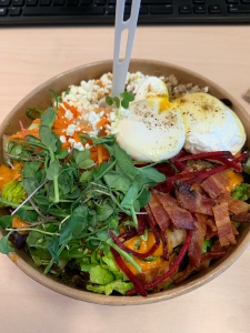 A top down image of a takeaway bowl with greens and poached eggs on top. 